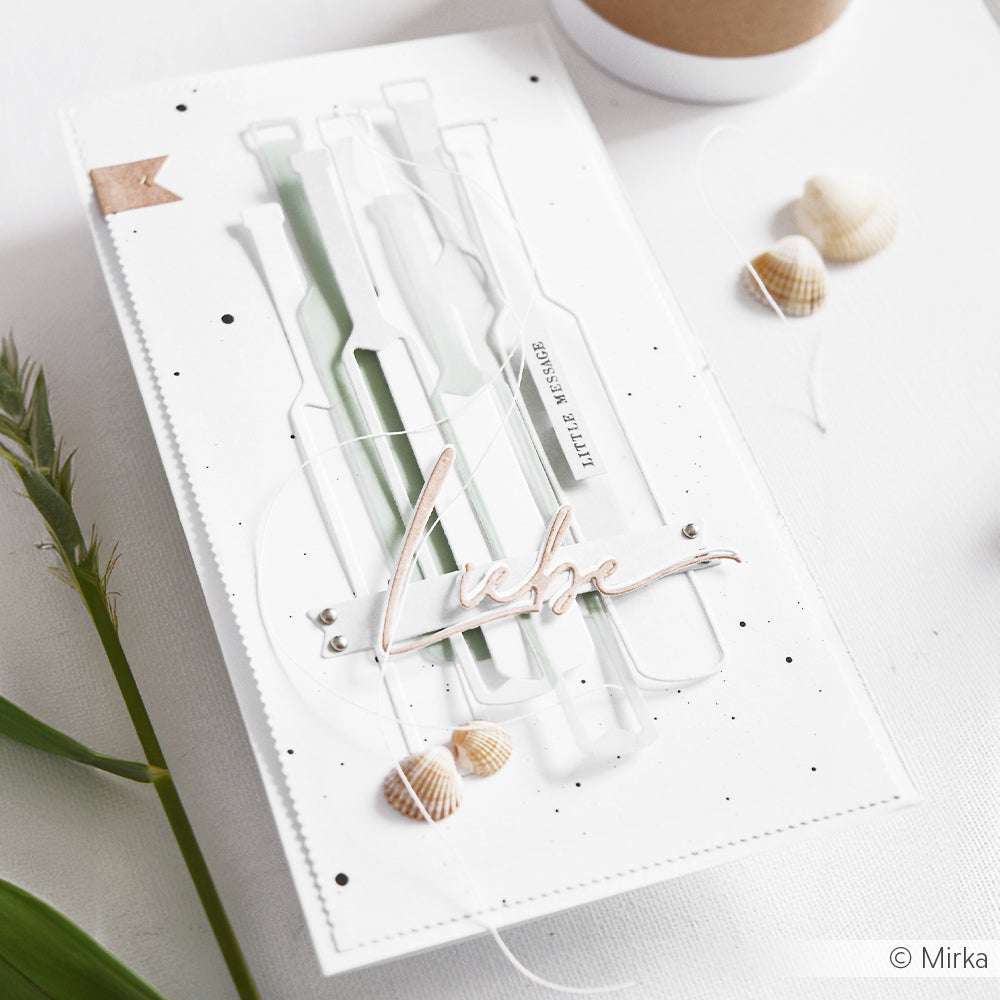 Handgefertigte Karte mit drei Flaschenausschnitten, die mit Alexandra Renke Stanzformen erstellt wurden, dem Text "Liebe", kleinen Muscheln und einem minimalen weißen Hintergrund.