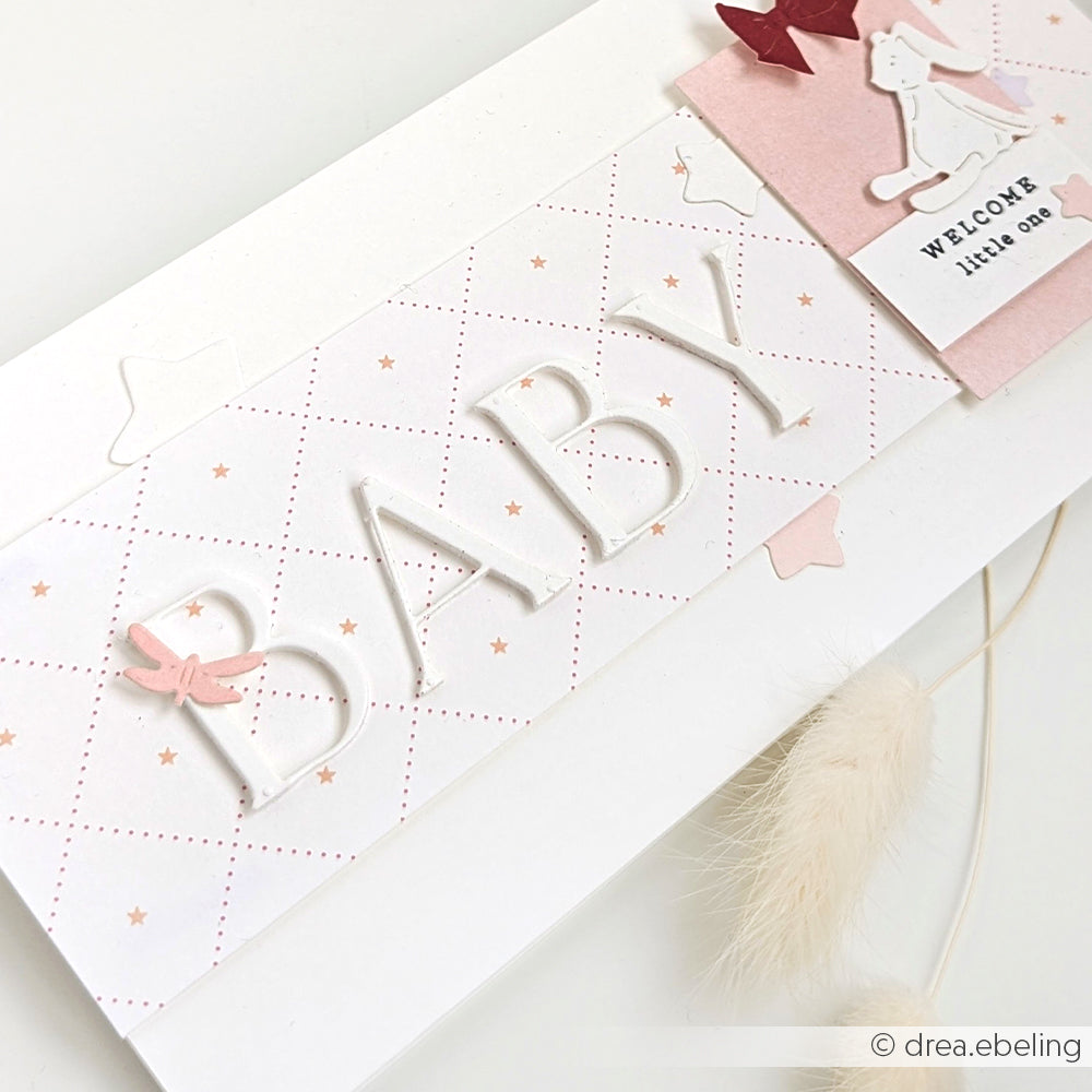 Handgemachte Babykarte von Alexandra Renke mit erhabenem BABY-Text, sanften Pastellfarben und einem "Welcome little one"-Anhänger mit einem Häschen.