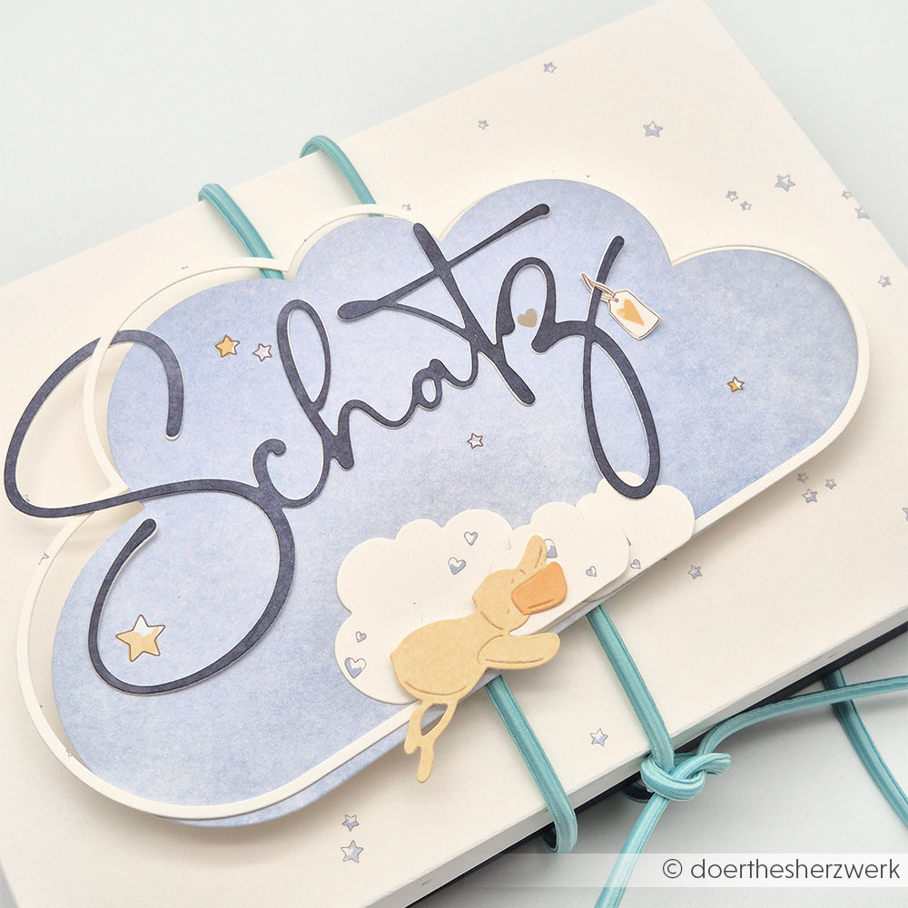 Eine wolkenförmige Karte von Alexandra Renke mit dem Schriftzug "Schatz", Sternen und einem kleinen schlafenden Bären auf blauem Hintergrund - perfekt für einzigartige Designpapierbasteleien mit Motivstanze oder DieCut Systemen.