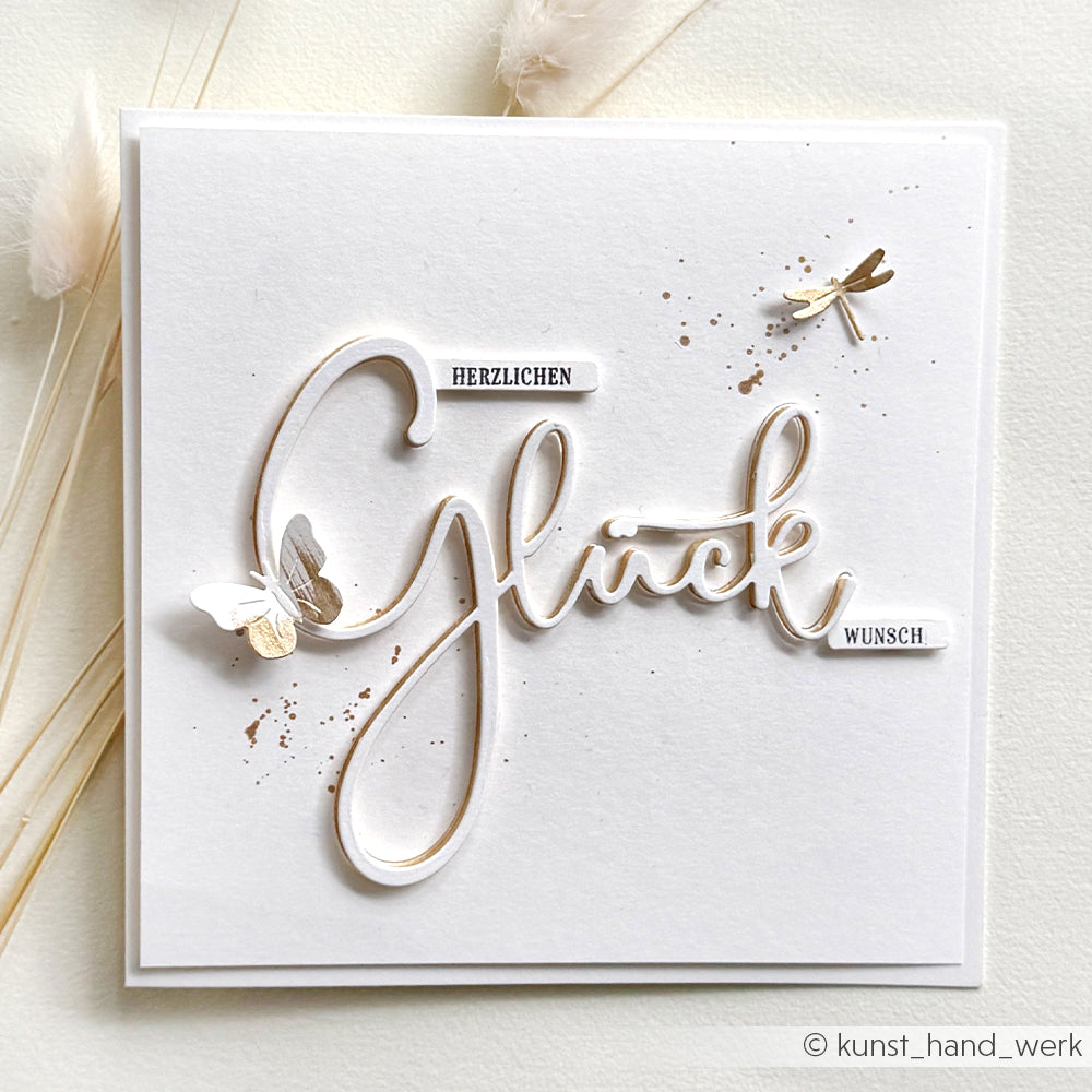 Weiße Alexandra Renke Grußkarte mit "Herzlichen Glückwunsch" in Schreibschrift, verziert mit Metallic-Schmetterlingen und einer Libelle, die mit der filigranen Motivstanze und den Dies gestaltet wurden.