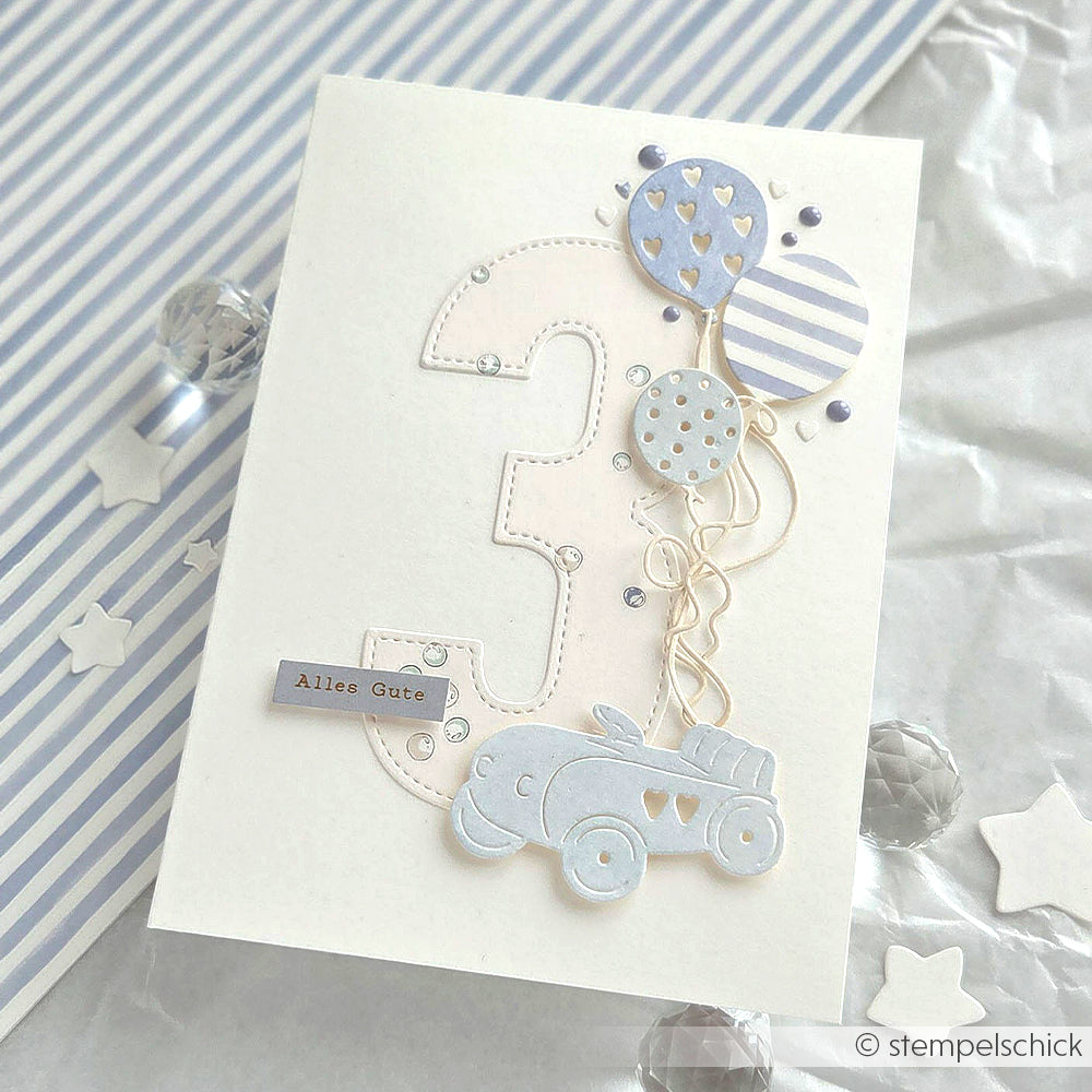 Grußkarte von Alexandra Renke mit einer großen Zahl 3, die mit der Motivstanze Zahlen ausgestanzt wurde, blauen Luftballons und einem Spielzeugauto auf gestreiftem und sterngemustertem Designpapier.