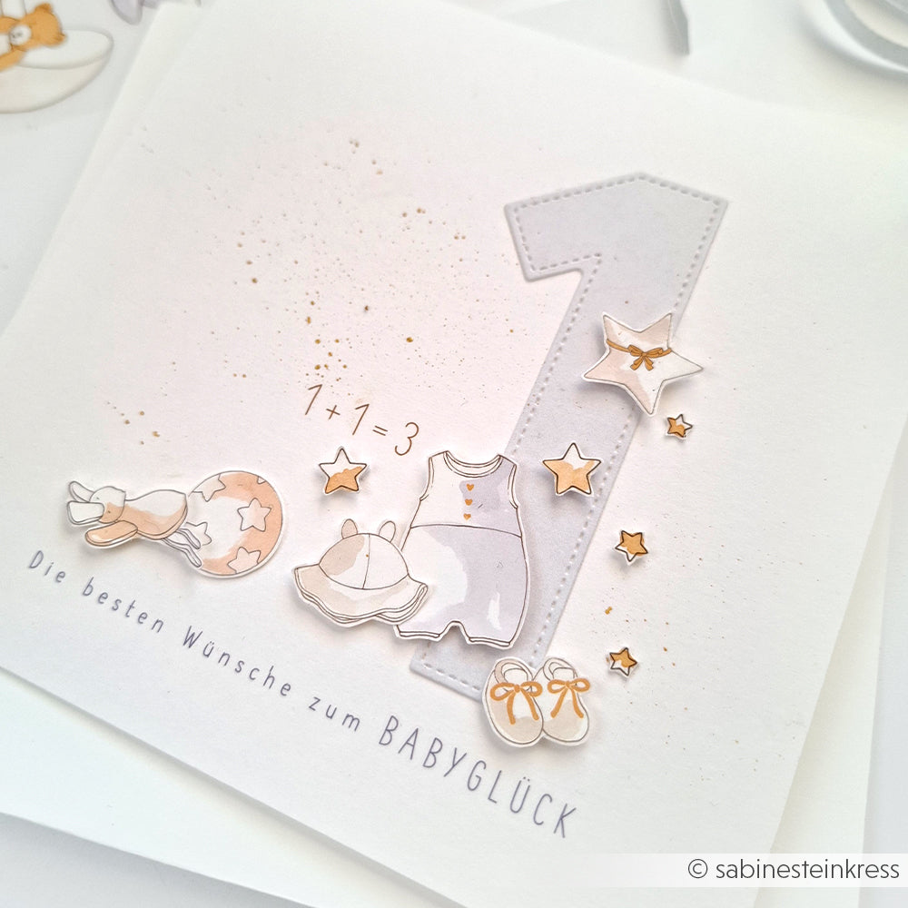 Grußkarte von Alexandra Renke mit Babyartikeln, einer großen Zahl 1, die mit Motivstanze Zahlen Dies hergestellt wurde, und deutschen Wünschen zur Ankunft eines neuen Babys.