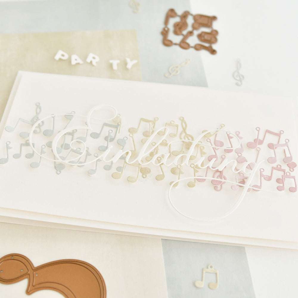 Eine handgefertigte Einladungskarte von Alexandra Renke aus Designpapier zeigt bunte Musiknoten und das Wort "Einladung", das mit einer kalligrafischen Stanze für Einladungsmotive hergestellt wurde.