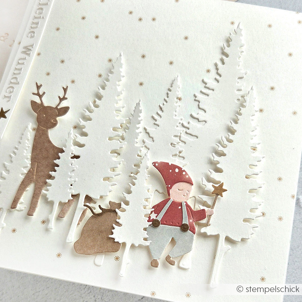 Eine festliche Karte von Alexandra Renke mit einem Gnom, zwei Rentieren und weißen Bäumen auf einem verschneiten Hintergrund mit goldenen Sternen.
