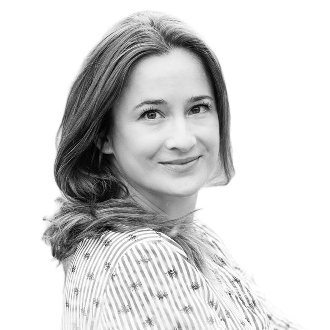 Frau mit langen Haaren, die ein gestreiftes Hemd trägt, lächelt und in die Kamera schaut, vor einem weißen Hintergrund.