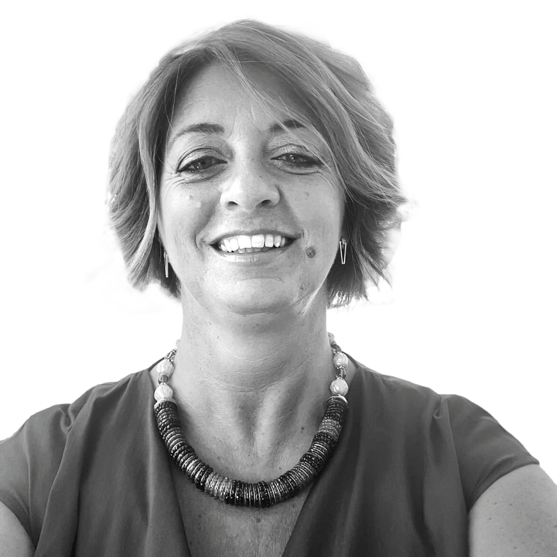 Lächelnde Frau mit kurzen Haaren, die eine Halskette und Ohrringe trägt, fotografiert vor einem schlichten weißen Hintergrund.