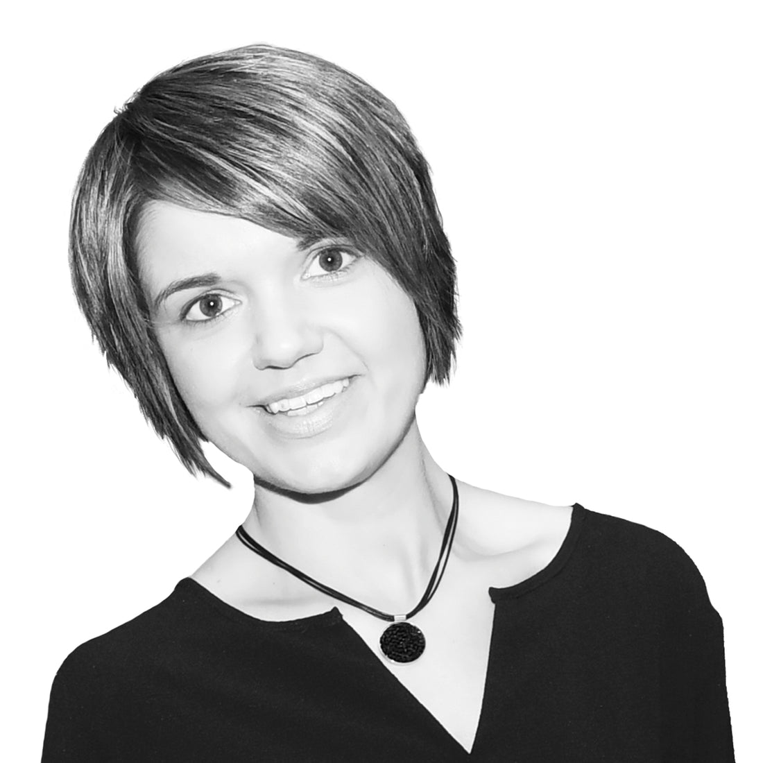 Lächelnde Frau mit kurzen Haaren und einer Halskette, die ein dunkles Oberteil trägt, auf weißem Hintergrund.