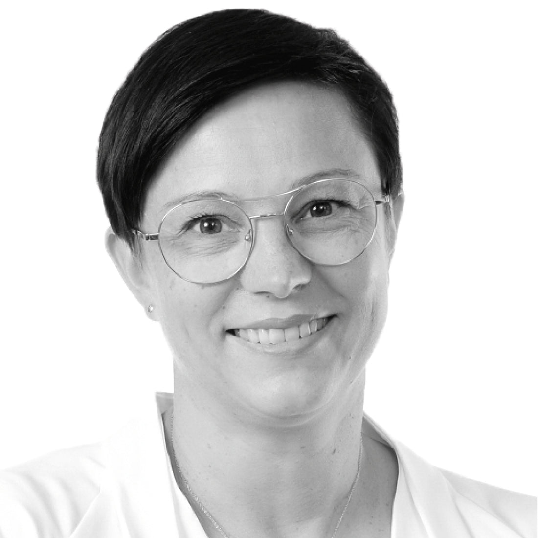 Lächelnde Frau mit kurzen dunklen Haaren, die eine Brille und ein weißes Oberteil trägt, auf weißem Hintergrund.