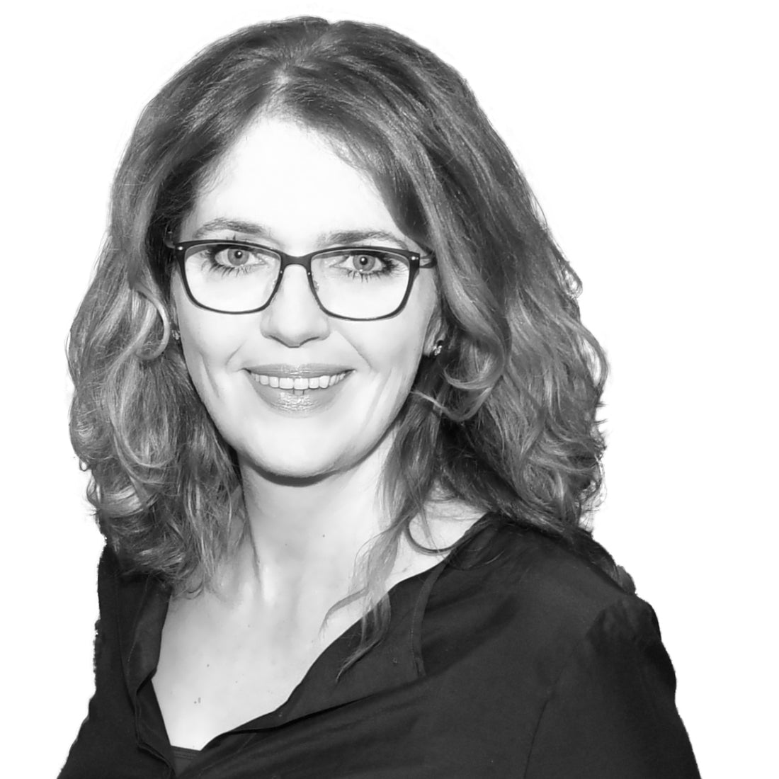 Frau mit gewelltem Haar und Brille, lächelnd, trägt ein dunkles Oberteil, in Schwarz-Weiß-Porträt auf weißem Hintergrund.