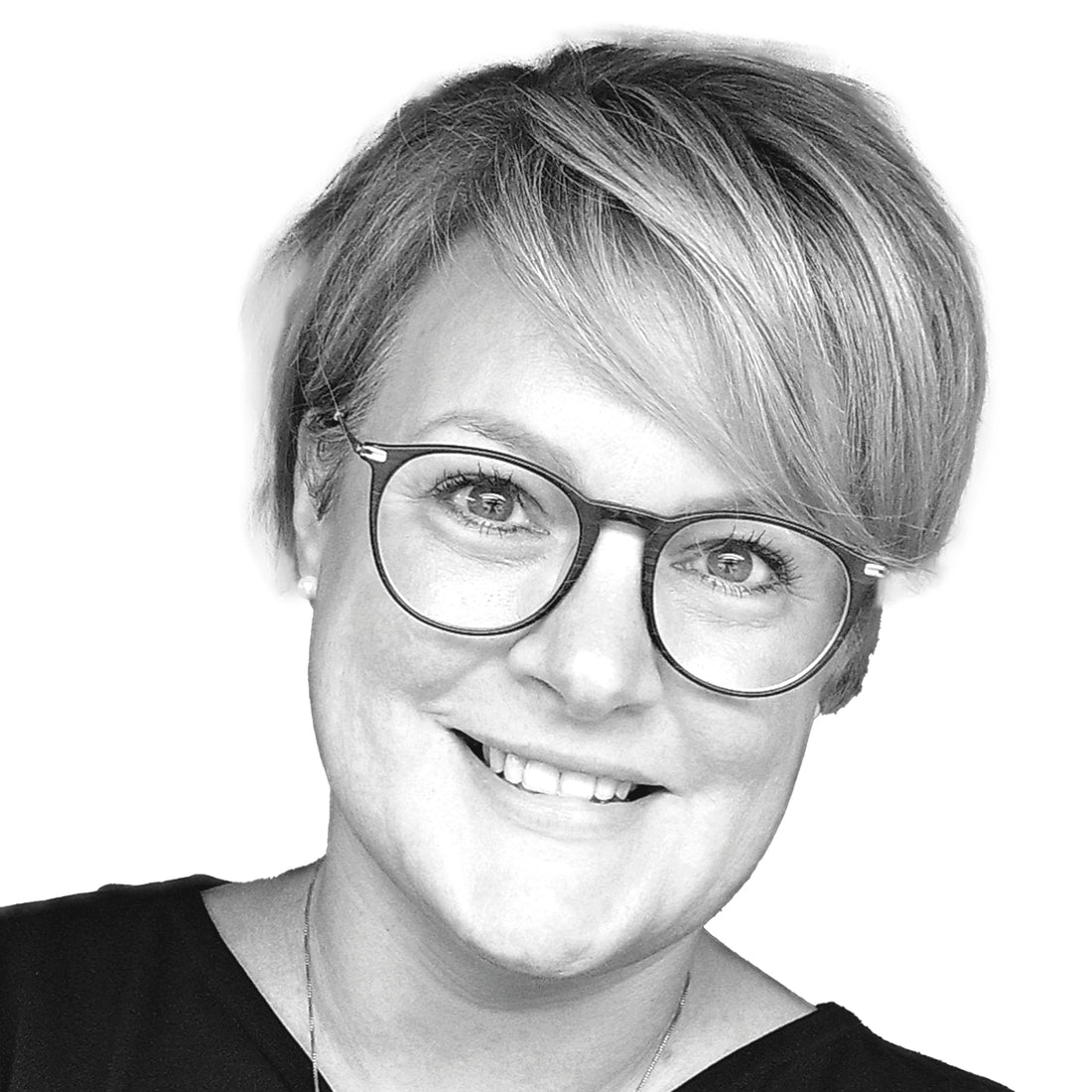 Lächelnde Frau mit kurzen blonden Haaren und runder Brille, die ein dunkles Oberteil trägt, vor einem weißen Hintergrund.