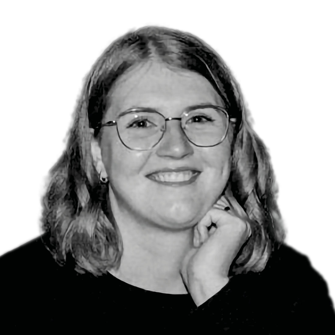 Eine Frau mit Brille und schulterlangem Haar lächelt und stützt ihr Kinn auf ihre Hand vor einem weißen Hintergrund.