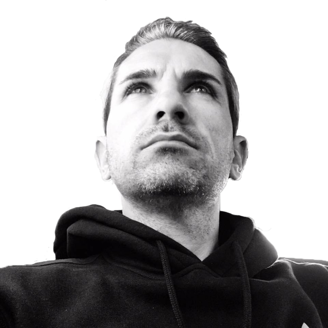 Mann im schwarzen Kapuzenpulli, der vor einem schlichten weißen Hintergrund nach oben schaut.