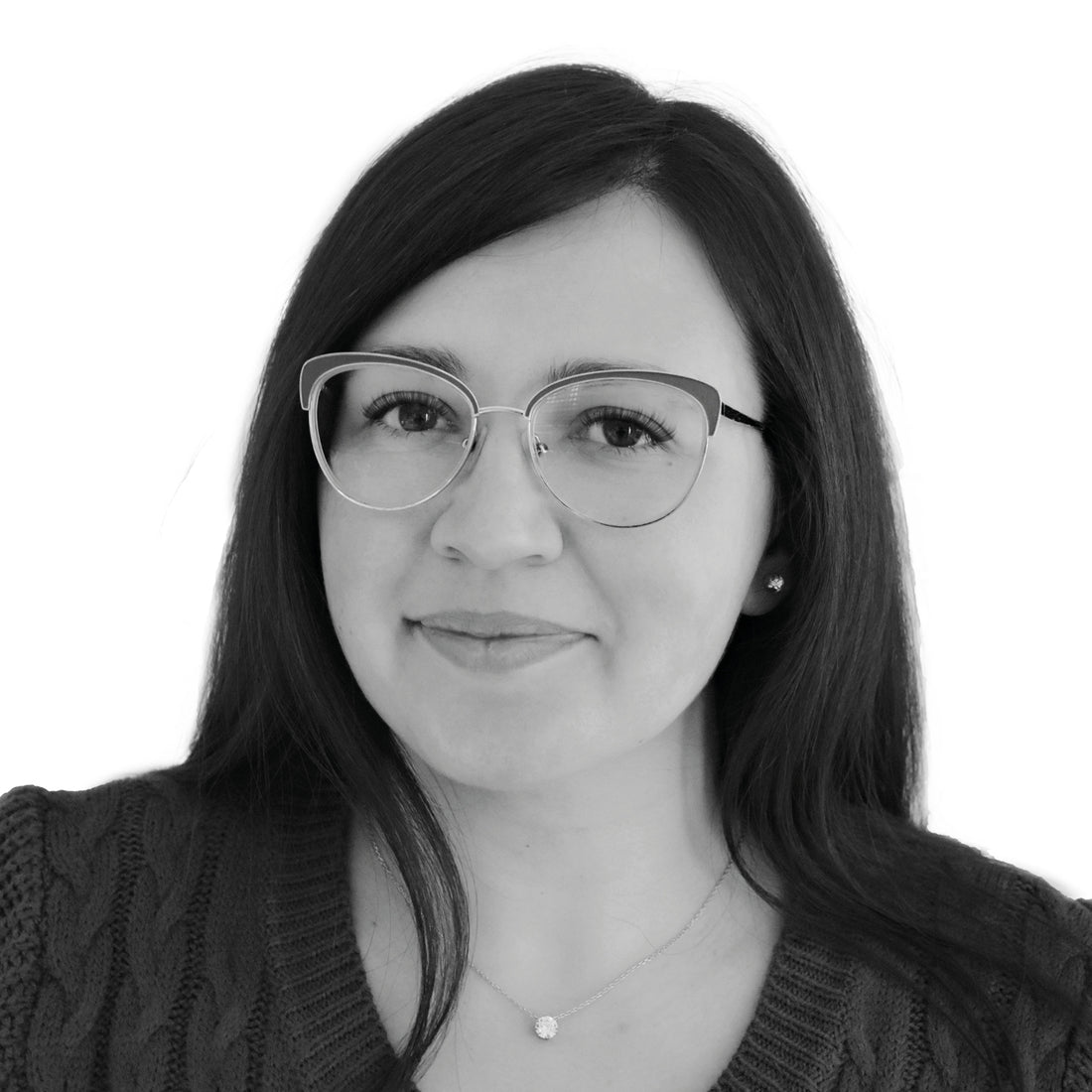 Frau mit langen dunklen Haaren, Brille und Pullover, die vor einem schlichten weißen Hintergrund sanft lächelt.