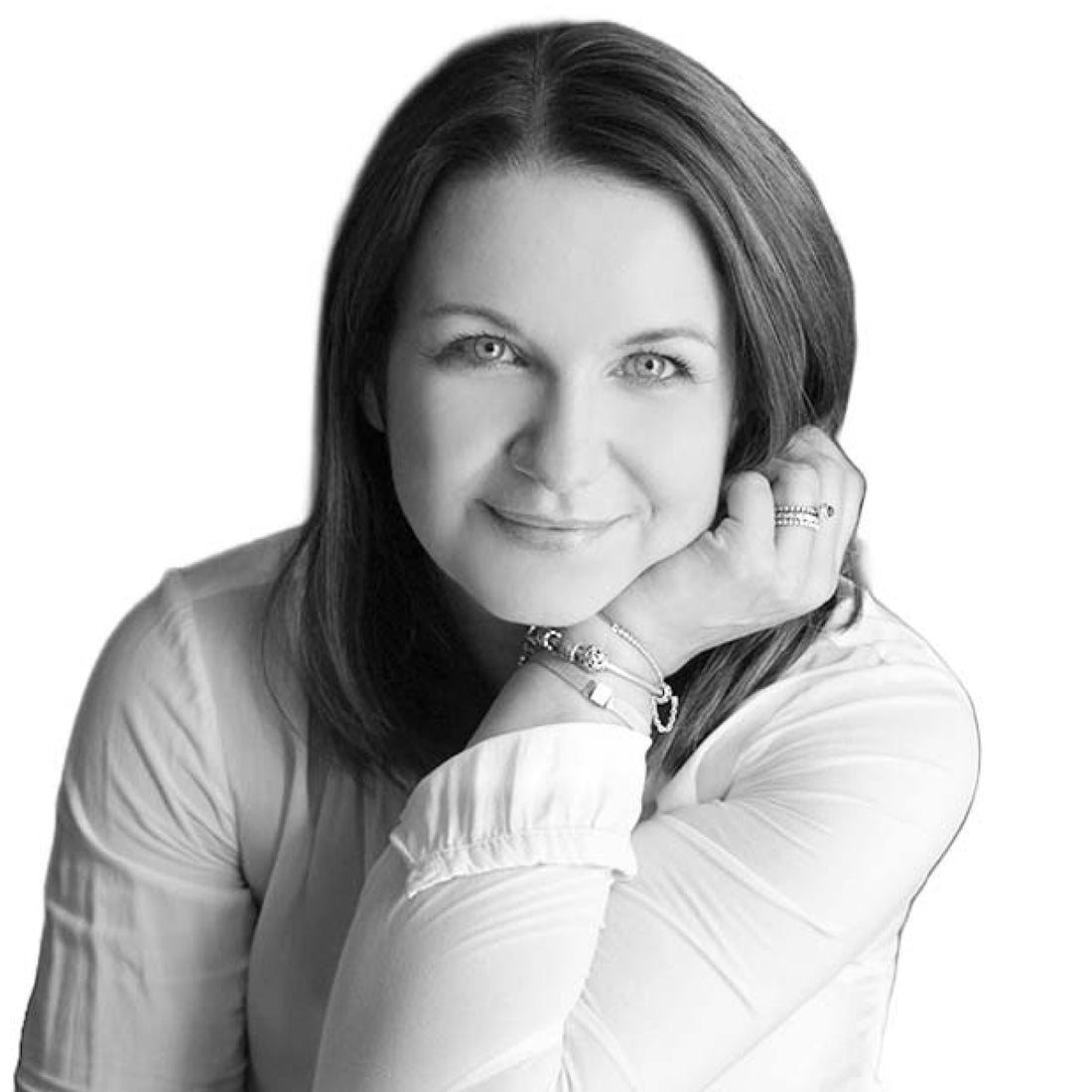 Frau mit glattem Haar, lächelnd, den Kopf auf die Hand gestützt, trägt eine helle Bluse und Armbänder.