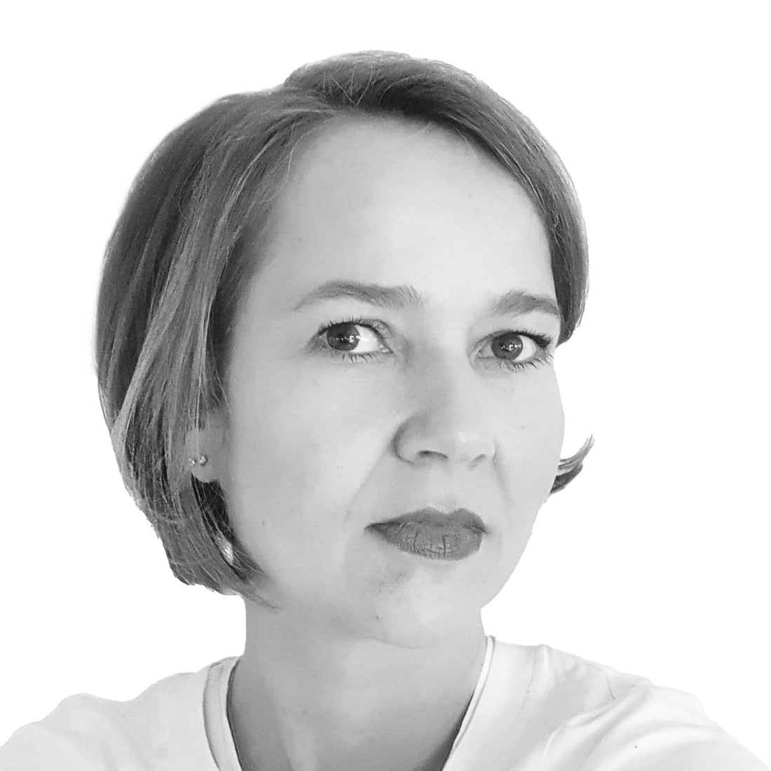 Schwarz-Weiß-Porträt einer Frau mit kurzen Haaren, die mit neutralem Gesichtsausdruck direkt in die Kamera schaut.