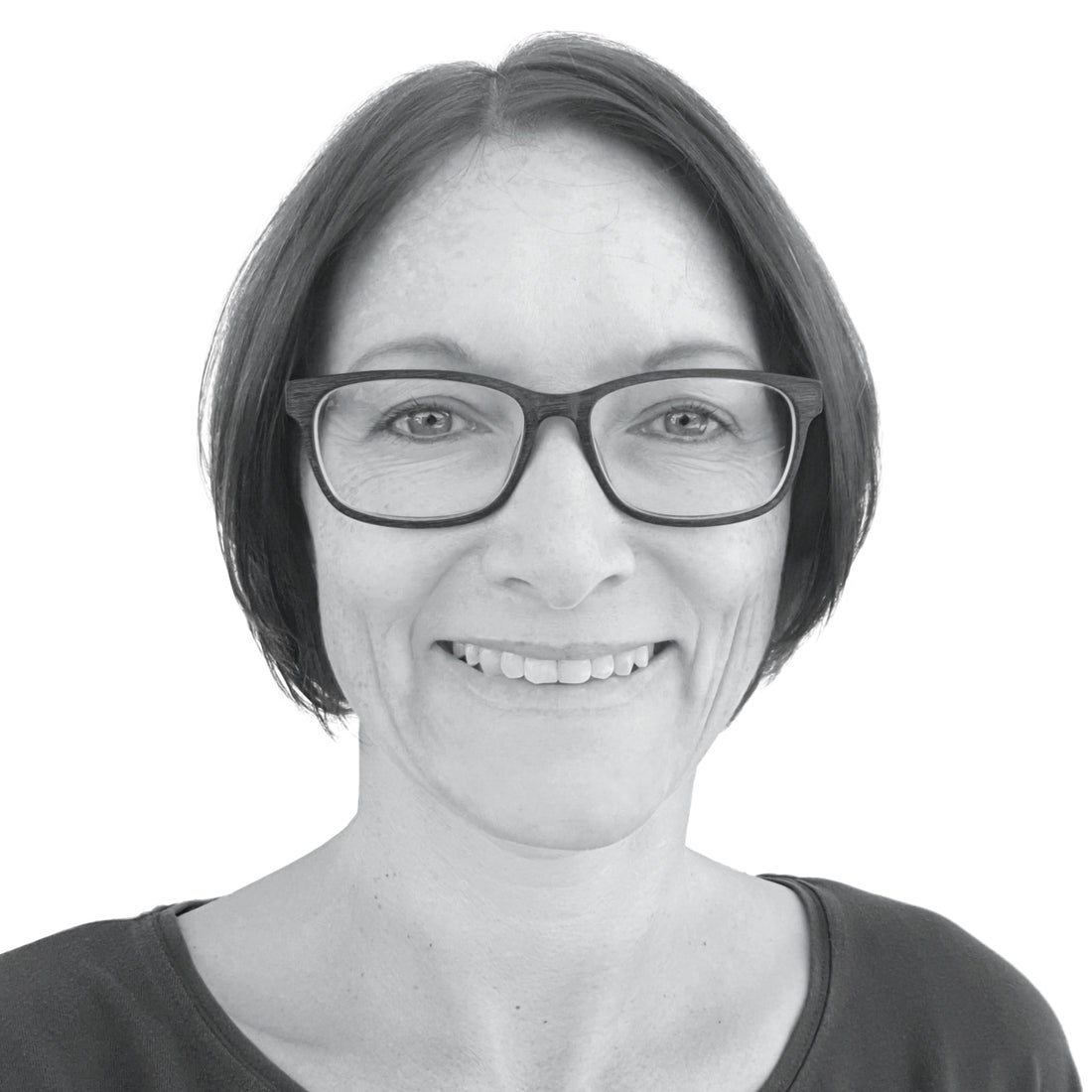 Lächelnde Frau mit kurzen dunklen Haaren und Brille, die ein dunkles Oberteil trägt, auf weißem Hintergrund.