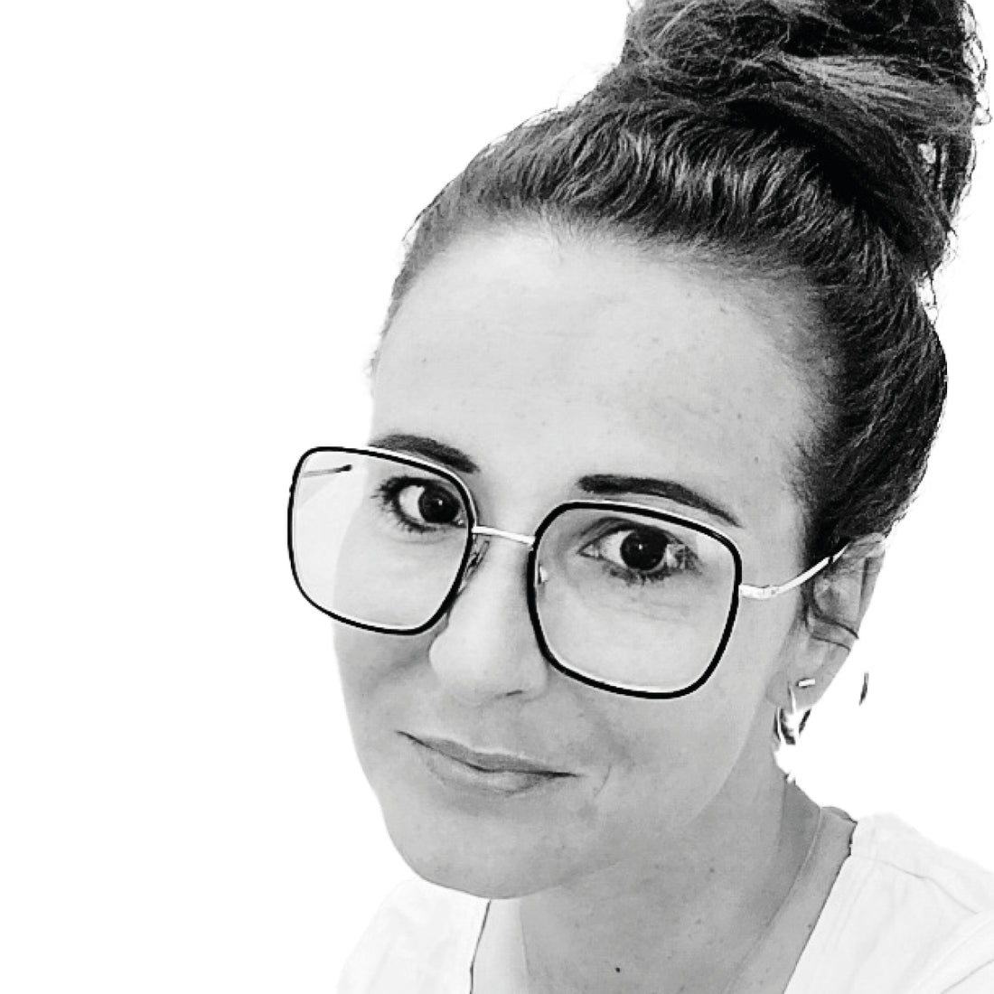 Frau mit großer Brille und Haarknoten, leicht lächelnd, auf einem Schwarz-Weiß-Foto.