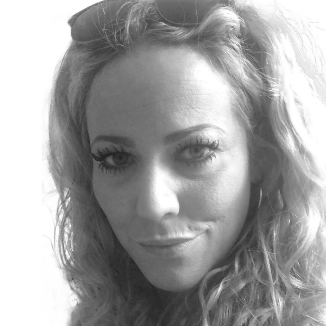 Schwarz-Weiß-Nahaufnahme einer Frau mit gewelltem Haar, Ohrringen und einer Sonnenbrille, die auf ihrem Kopf ruht.