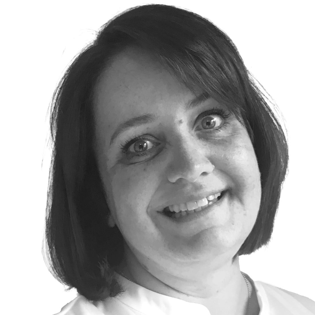 Frau mit kurzen dunklen Haaren, lächelnd, mit einem hellen Oberteil, fotografiert vor einem schlichten weißen Hintergrund.