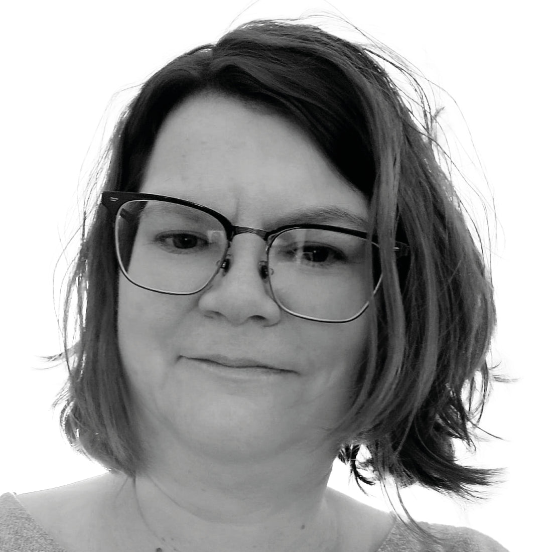 Frau mit schulterlangem Haar und Brille, leicht nach unten blickend, in schwarz-weiß.