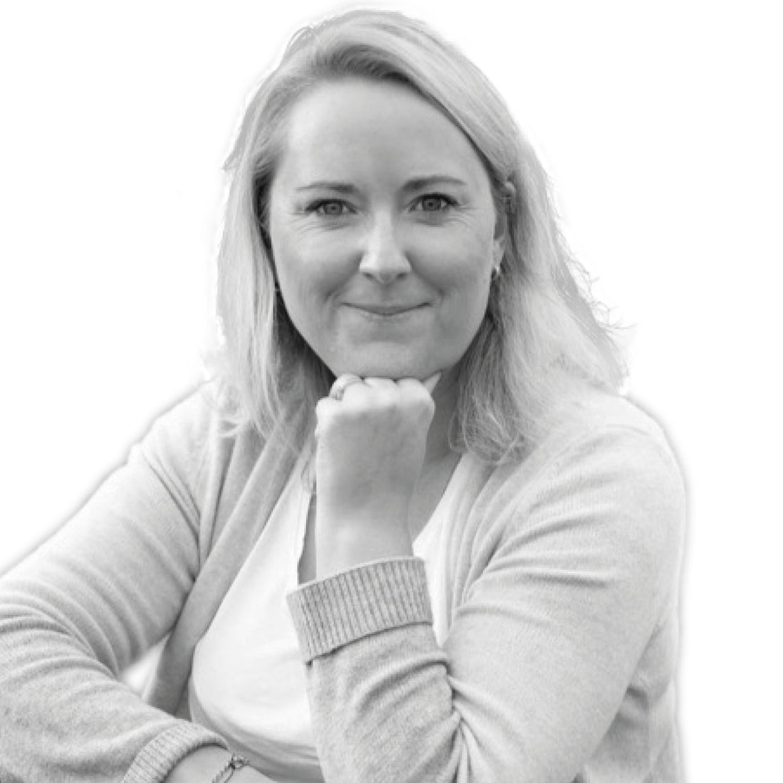 Frau mit hellem Haar, lächelnd, das Kinn auf die Hand gestützt, trägt einen hellen Pullover über einem weißen Hemd.