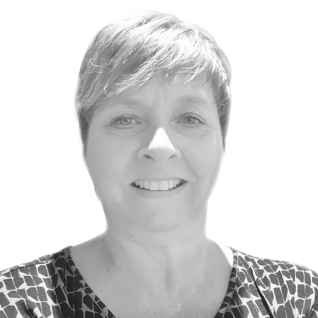 Lächelnde Frau mit kurzen hellen Haaren, die ein gemustertes Oberteil trägt, vor einem weißen Hintergrund.