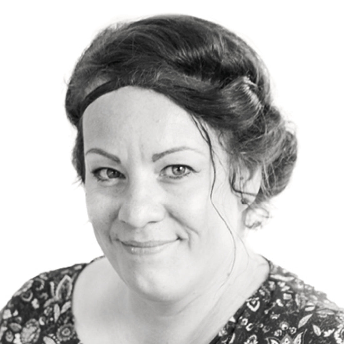 Frau mit dunklem, gewelltem Haar und gepunktetem Oberteil, die vor einem weißen Hintergrund leicht lächelt.