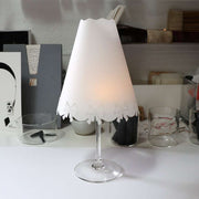 Das Weinglas Alexandra Renke mit einem Lampenschirm aus Papier mit ausgeschnittenen Schleifen wird zu einer charmanten Tischleuchte, deren transparente Lampenschirme einen sanften, dekorativen Schein verbreiten.