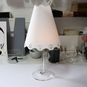 Ein Weinglas mit einem dekorativen Papier-Lampenschirm von Alexandra Renke steht auf einem weißen Schreibtisch, umgeben von Zeichenmaterialien - eine elegante Dekoration, inspiriert von stilvollen Tischlampen.