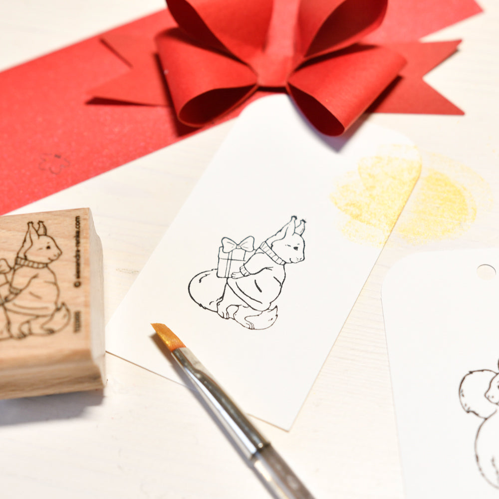Ein Eichhörnchen-Stempel mit einem Geschenk, einem Pinsel und einer roten Papierschleife.