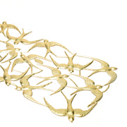 Die goldene Metallwandkunst zeigt mehrere Schwalben im Flug, die in einem ineinandergreifenden Muster auf weißem Hintergrund angeordnet sind - ein elegantes Dekoelement, das jedem Raum eine anmutige Bewegung verleiht.