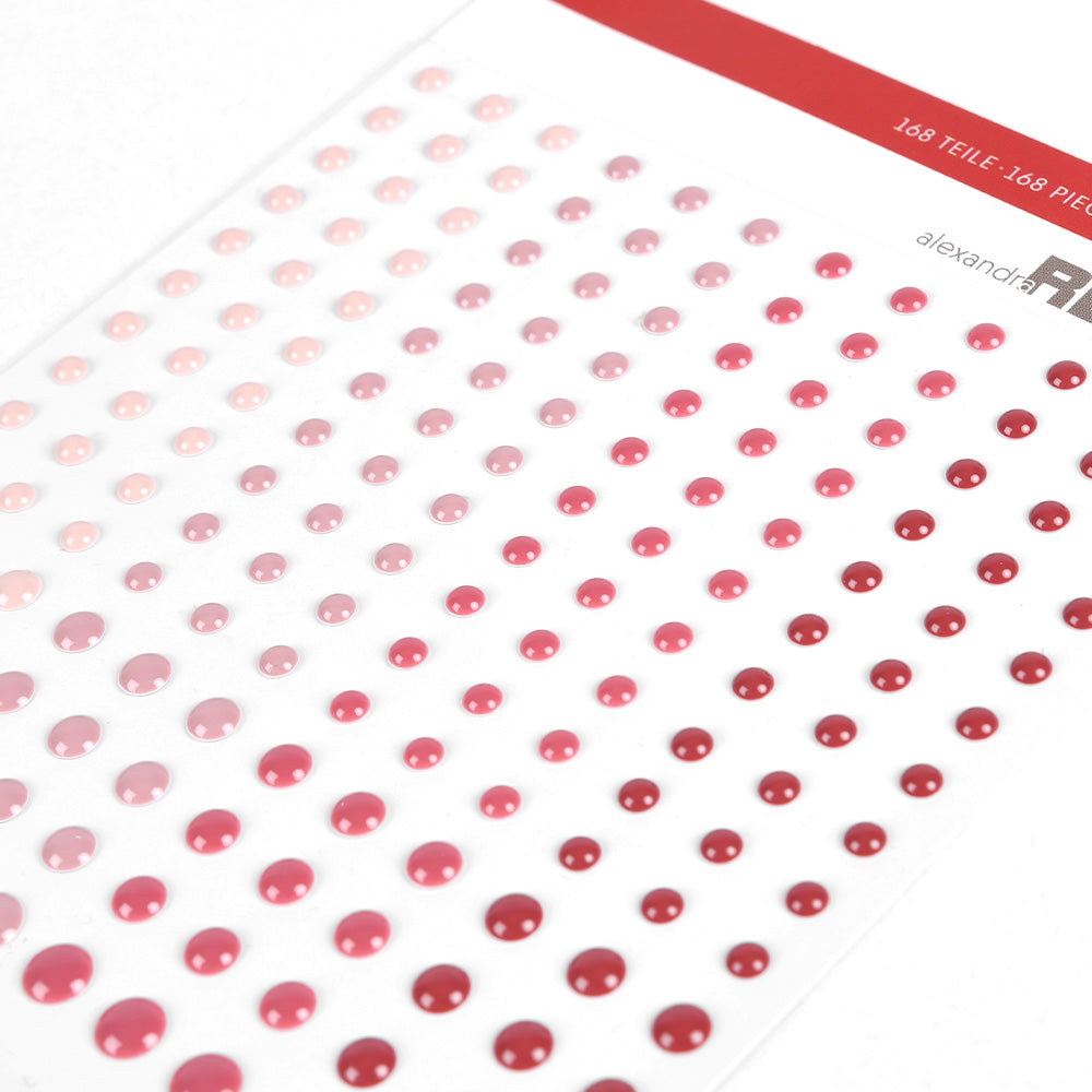 Ein Bogen selbstklebender Emaille-Punkte von Alexandra Renke in Rot-, Rosa- und Altrosa-Tönen, in Reihen angeordnet und in verschiedenen Größen - ideal für die Kartengestaltung.