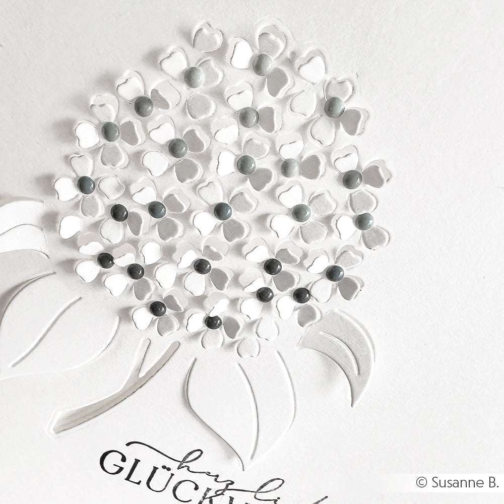 Weißes Strukturpapier von Alexandra Renke mit einer Hortensie mit erhabenen Blütenblättern, grauen Emaillepunkten und blättrigen Stängeln - eine originelle Kartengestaltung mit Akzenten in Kosmosblau.