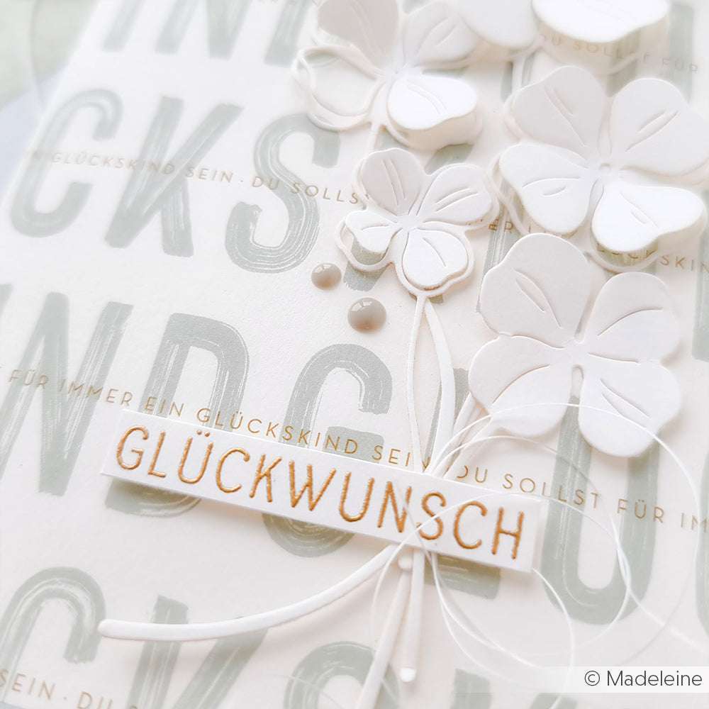 Weiße Grußkarte von Alexandra Renke mit goldfarbenem "GLÜCKWUNSCH", zartem Hintergrundtext auf warmem Grau und feinen Enamel Dots - ideal für besondere Anlässe.