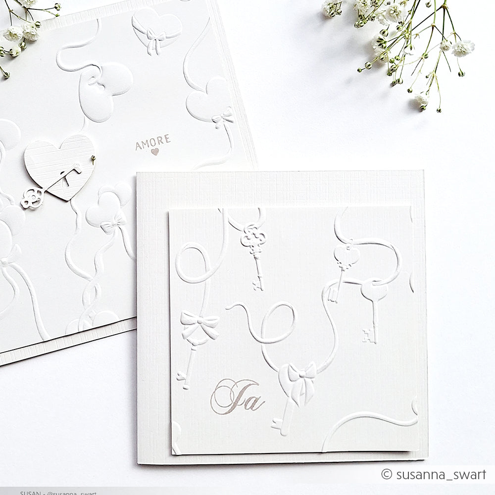 Zwei elegante weiße Prägekarten von Alexandra Renke aus hochwertigen Designpapieren und Prägefolder mit Schlüssel-, Schleifen- und Herzmotiven und zarten weißen Blumen.