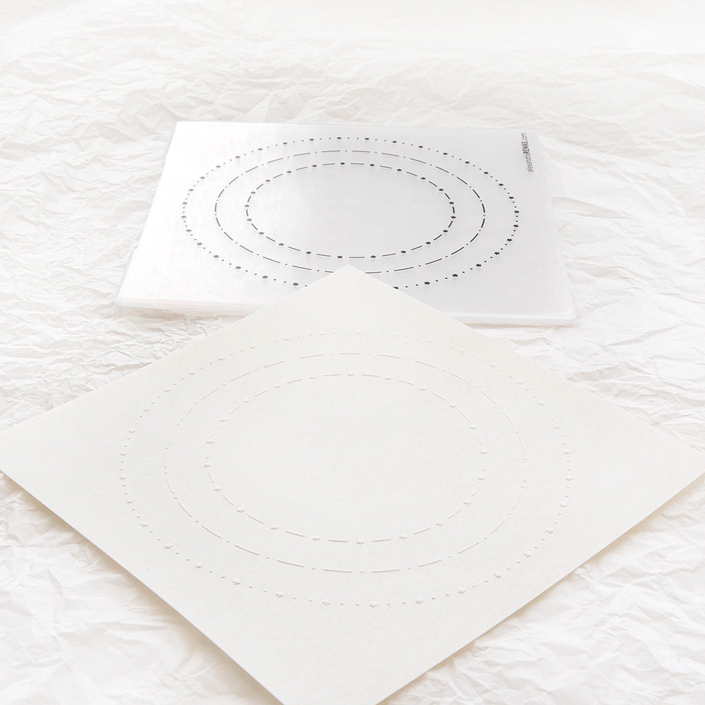 Zwei Papierbögen mit konzentrischen gepunkteten Ovalen, die mit dem Alexandra Renke Cut & Emboss Folder hergestellt wurden, liegen auf einer strukturierten weißen Oberfläche.