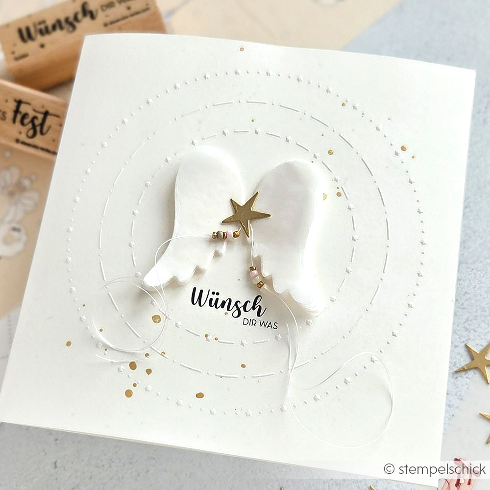 Die handgefertigte Karte von Alexandra Renke zeigt weiße Engelsflügel, einen goldenen Stern, goldene Perlen und den deutschen Text "Wünsch dir was", der mit einem Cut & Emboss Folder mit detaillierter Textur für ein wunderschönes, elegantes Finish hergestellt wurde.