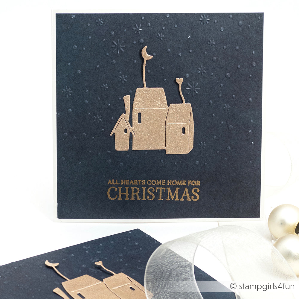 Marineblaue Karte mit goldenen Häusern und der Prägung "All hearts come home for Christmas". Mit dem Prägefolder Alexandra Renke Zarter Flockentanz wurde ein dezentes Schneeflockenmuster geprägt.