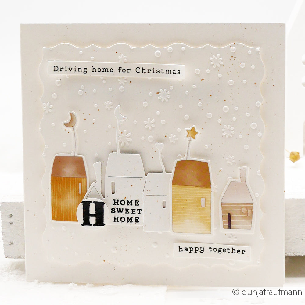 Handgemachte Karte mit einer Reihe von Häusern, Schneeflocken und der Botschaft "Driving home for Christmas and happy together". Festliche Textur mit dem Prägefolder Alexandra Renke Zarter Flockentanz.