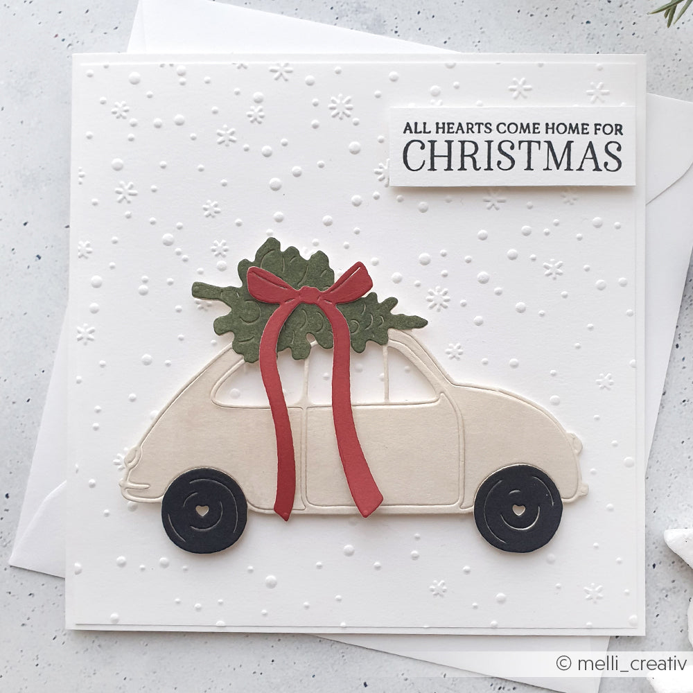 Handgefertigte Weihnachtskarte von Alexandra Renke mit einem Auto mit Baum und roter Schleife sowie der Botschaft "ALL HEARTS COME HOME FOR CHRISTMAS", hergestellt mit dem Zarter Flockentanz-Prägefolder für festliche Textur und Charme.