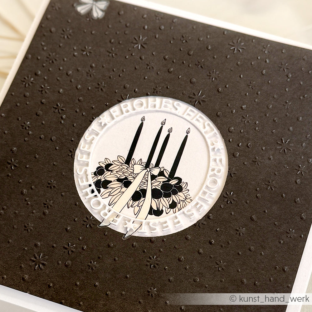 Schwarze Karte, gestaltet mit dem Schneide- und Prägefolder von Alexandra Renke, mit vier schwarzen Kerzen, Blumen und dem Schriftzug "Frohes Fest", der einen Kreis um das Design bildet.