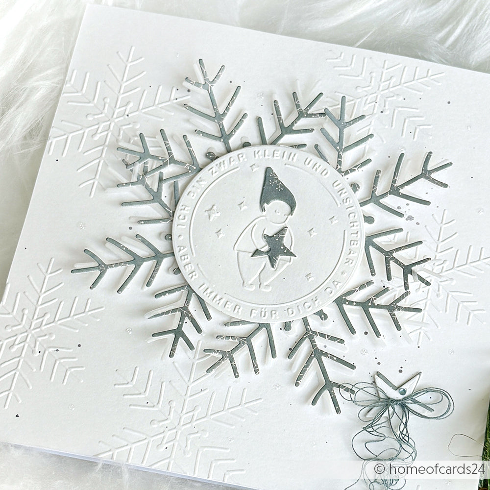 Diese weiße Weihnachtskarte von Alexandra Renke, die mit dem Cut & Emboss Folder erstellt wurde, zeigt geprägte Schneeflocken, eine große silberne Schneeflocke und ein Kind in Winterkleidung, das einen Stern hält.