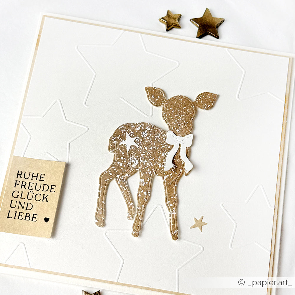 Grußkarte von Alexandra Renke mit einem goldenen Glitzerhirsch, drei goldenen Sternen, geprägten Sternen aus dem Prägefolder Sterne und einer deutschen Botschaft auf der linken Seite.