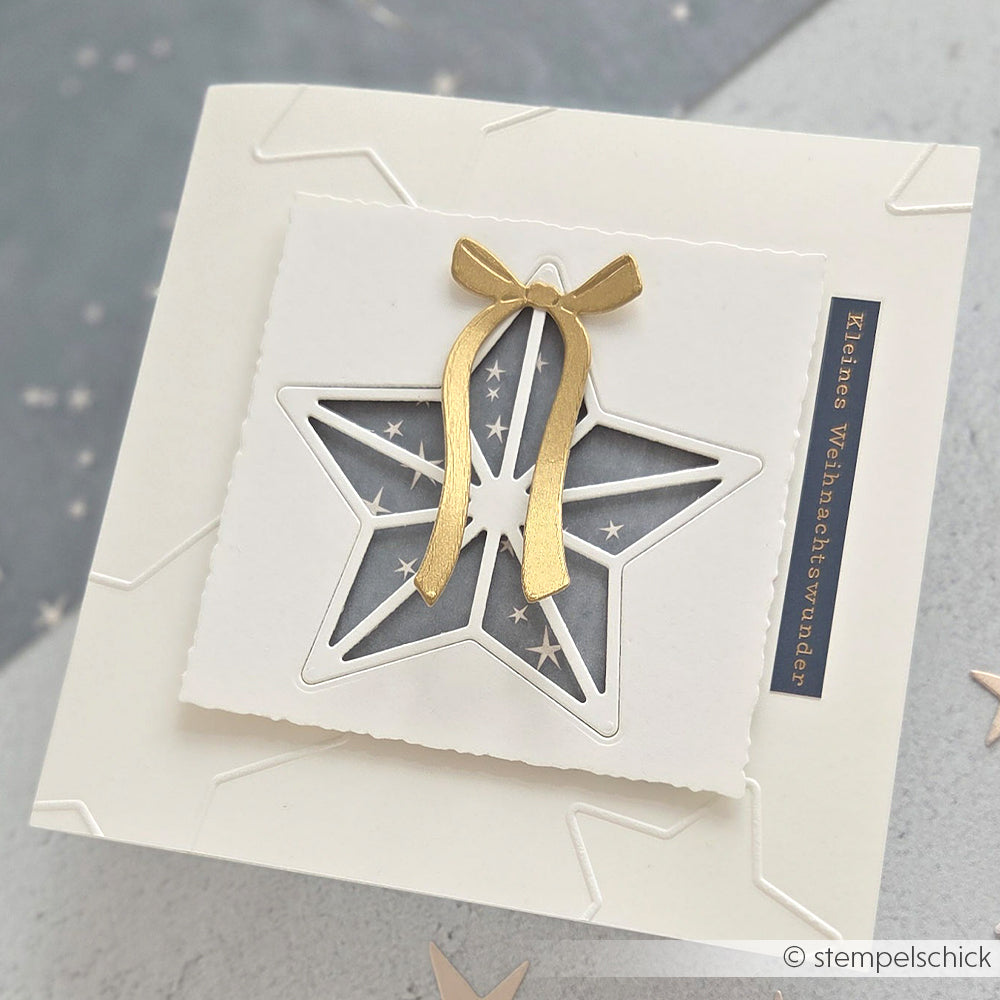 Quadratische weiße Karte von Alexandra Renke mit einem Sternausschnitt, goldenem Band, kleinen geprägten Sternen aus dem Cut & Emboss Folder und einem deutschen Textetikett auf der rechten Seite.