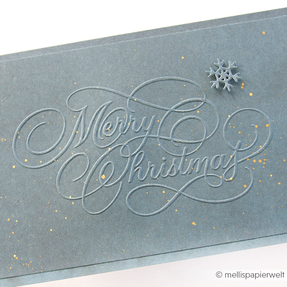 Graue Karte von Alexandra Renke mit "Frohe Weihnachten" in eleganter Schrift und einer kleinen Schneeflocke als Akzent, hergestellt mit einem Prägefolder für zusätzliche Dimension.