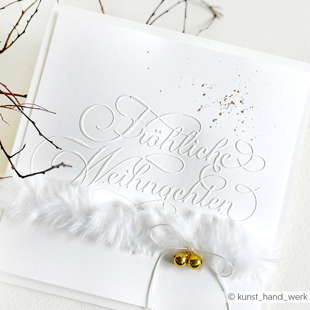 Weiße Weihnachtskarte von Alexandra Renke mit geprägtem "Fröhliche Weihnachten", goldenen Sprenkeln, weichem weißem Pelzbesatz und zwei goldschimmernden Glöckchen.