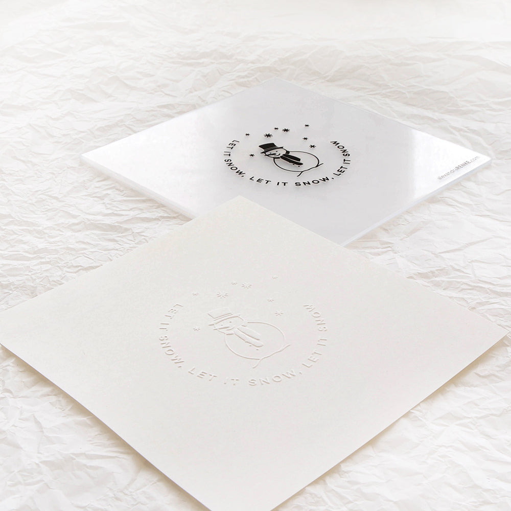Zwei quadratische Karten von Alexandra Renke mit dem Design Let it Snow - eine in Schwarz auf Weiß und eine, die mit einem Embossing-Folder elegant auf cremefarbenem Papier geprägt wurde.