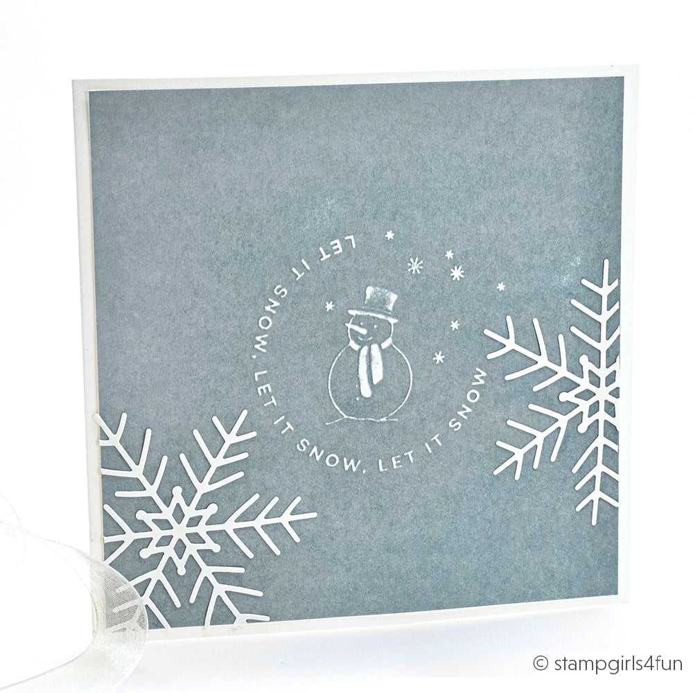 Die quadratische Winterkarte von Alexandra Renke wurde mit dem Cut & Emboss Folder erstellt und zeigt einen Schneemann, Schneeflocken und "Let it snow" in einem Kreis auf blauem Hintergrund.