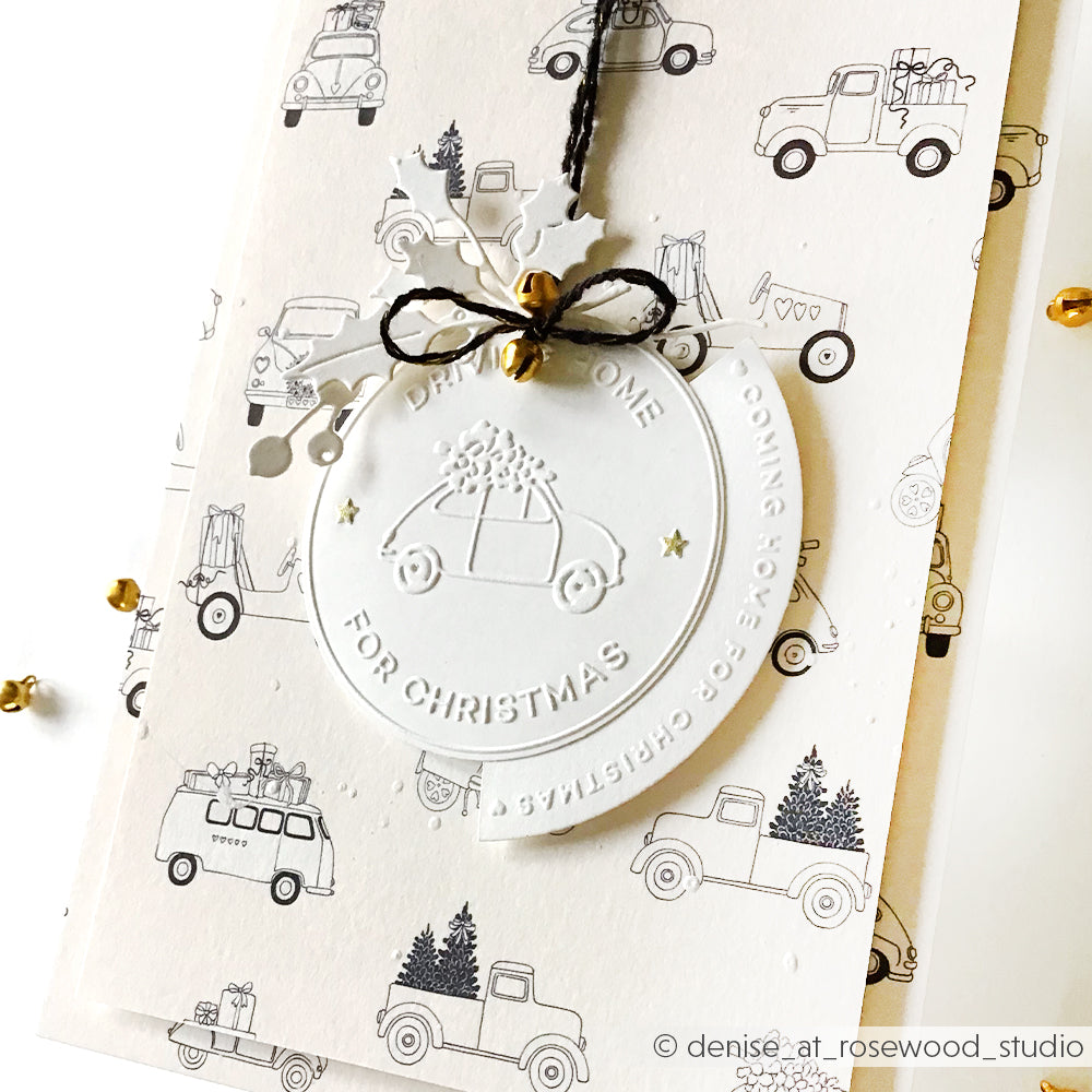 Das weiße Weihnachtsornament von Alexandra Renke zeigt ein geprägtes Auto und einen Baum, die mit schwarzer Schnur auf festlichem Autopapier zusammengebunden sind - perfekt, um Ihren bevorzugten Cut & Emboss Folder hervorzuheben oder die Stimmung "Driving home for Christmas" zu erzeugen.