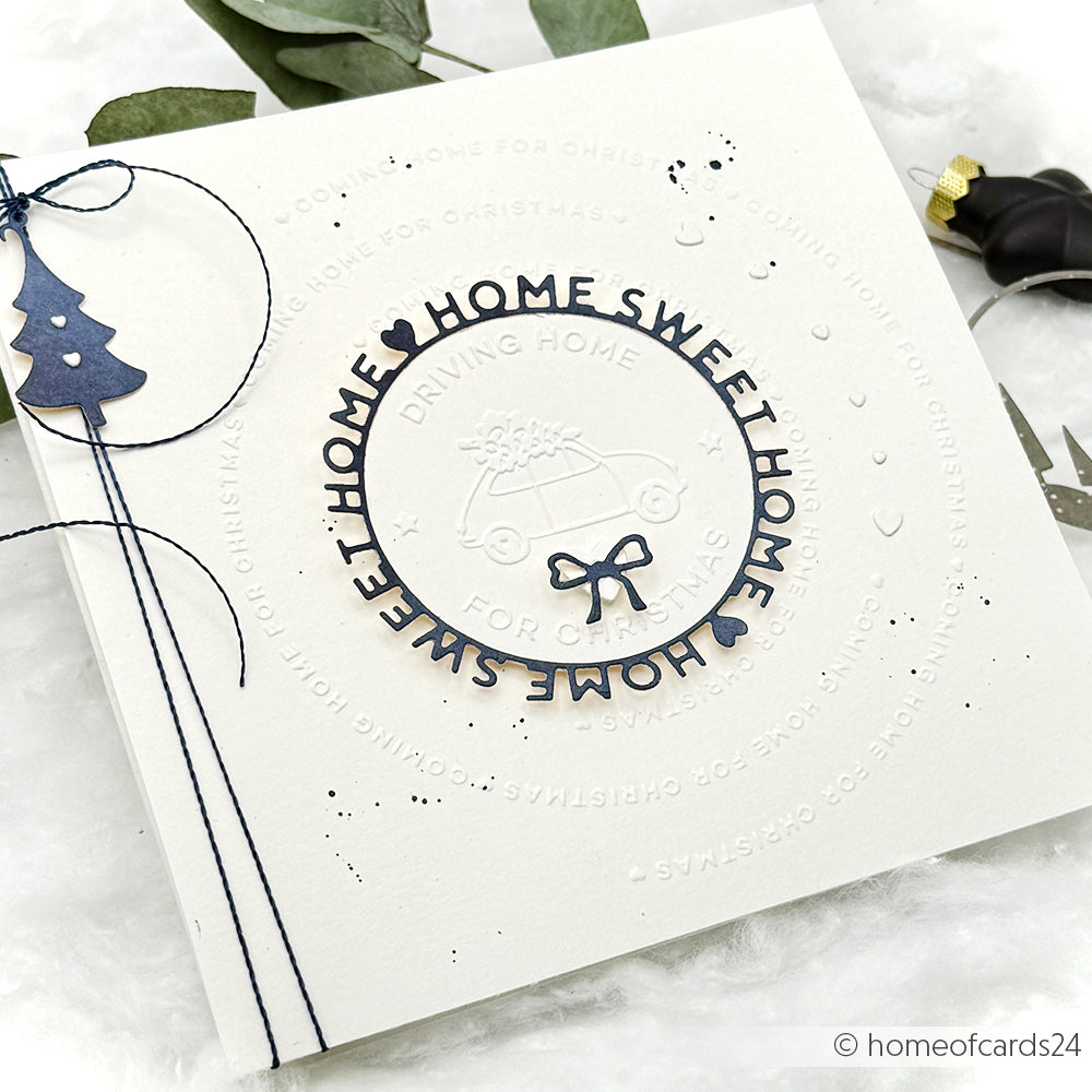 Die quadratische weiße Karte von Alexandra Renke wurde mit dem Cut & Emboss Folder gestaltet und zeigt den geprägten Text "HOME SWEET HOME", ein Auto mit Baum, eine marineblaue Schleife und eine blaue Schnur - ideal für die Fahrt nach Hause zu Weihnachten.